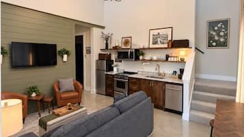A modern living room with a sofa, a dining table, and a kitchen in the background.