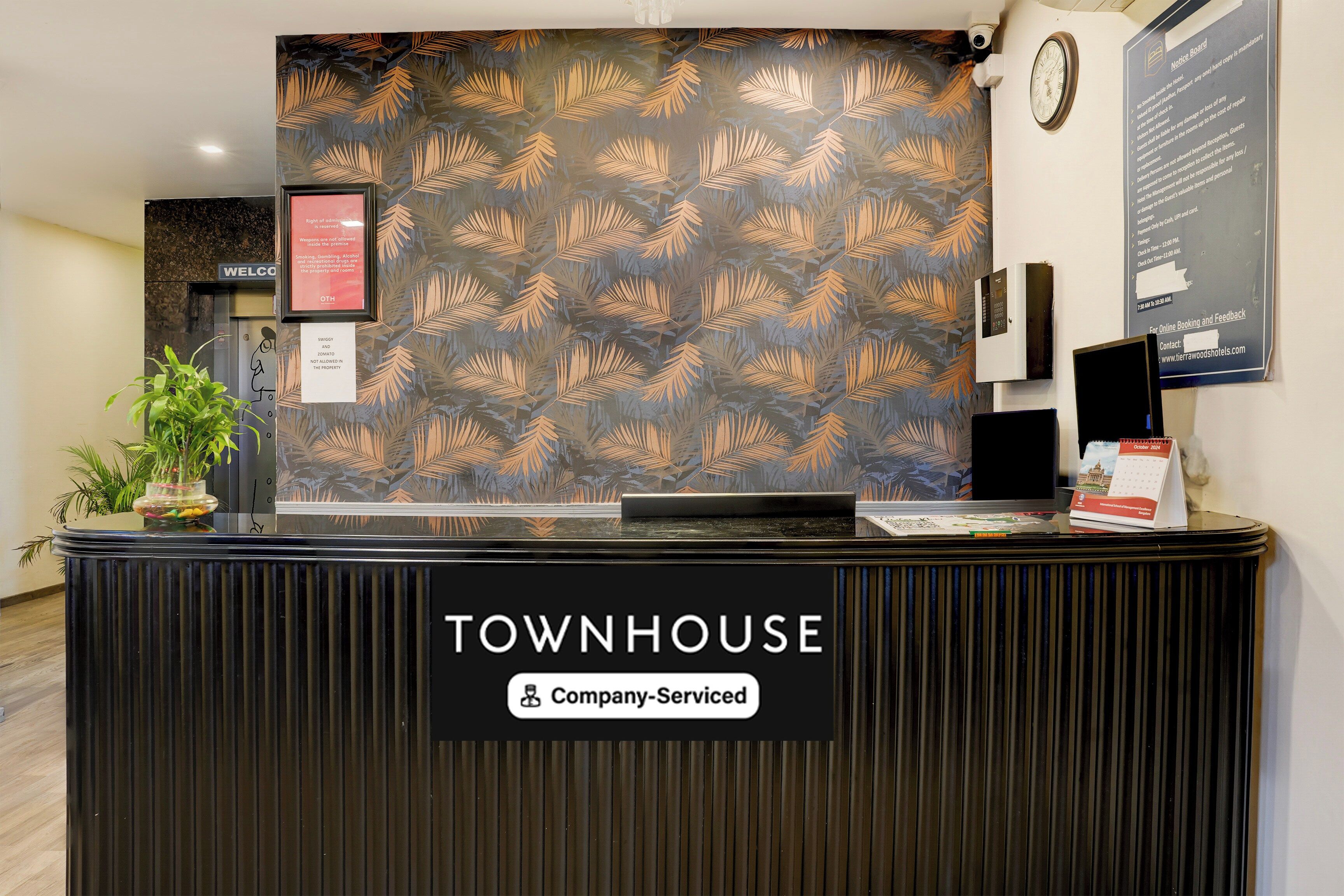 Una recepción con un cartel que dice 'TOWNHOUSE', un tablón de anuncios y un reloj.