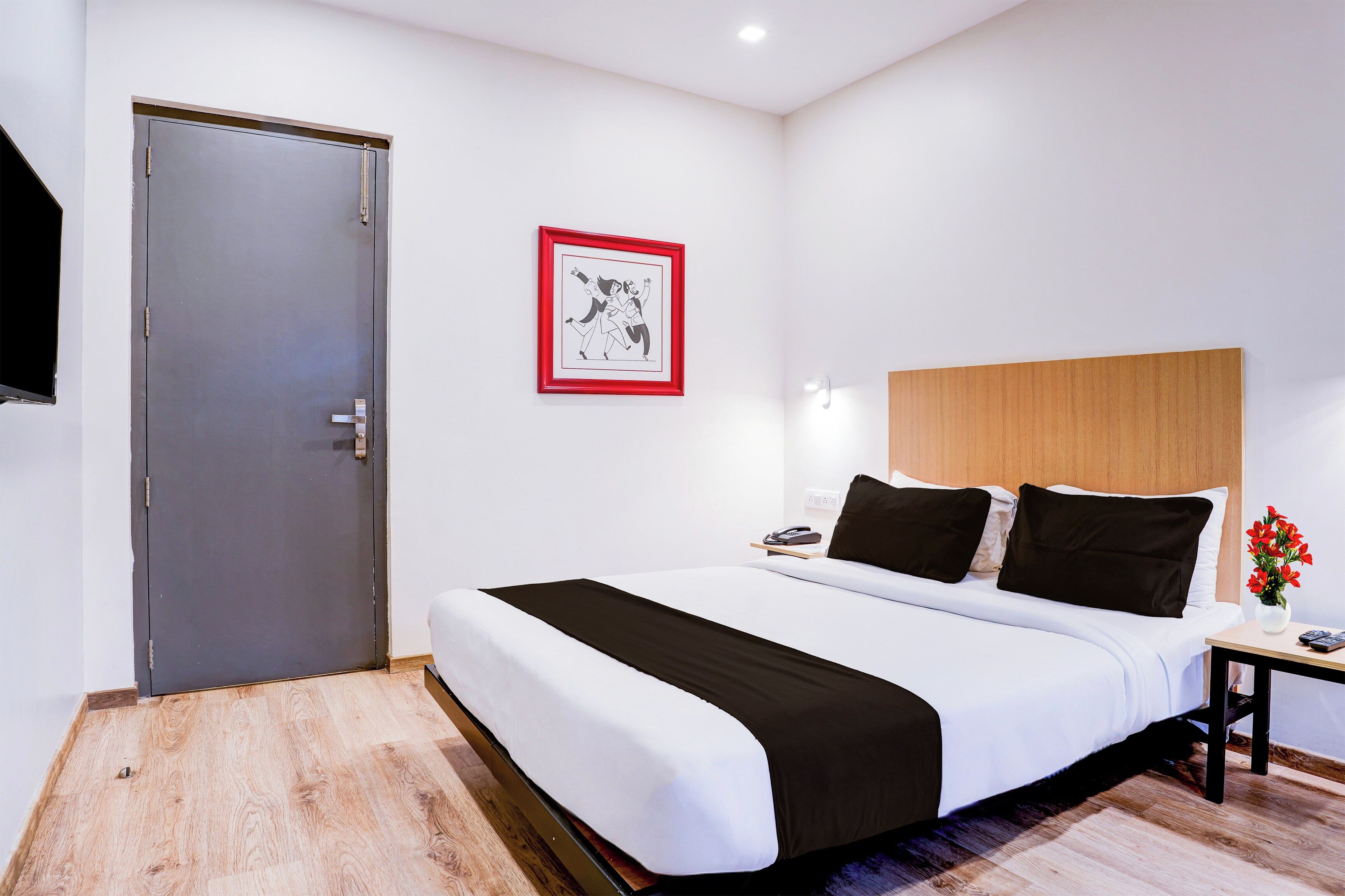 Una habitación de hotel con cama, mesita de noche, teléfono, un cuadro enmarcado y una puerta.