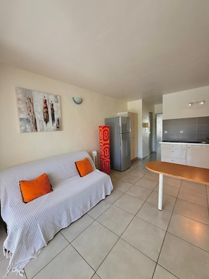 A modern living room with a sofa, a dining table, a kitchen area with a refrigerator, and a wall-mounted artwork. - Caribbean Getaway in Le Gosier, Sea View • Pool • WiFi • Near Restaurants (Le Gosier)