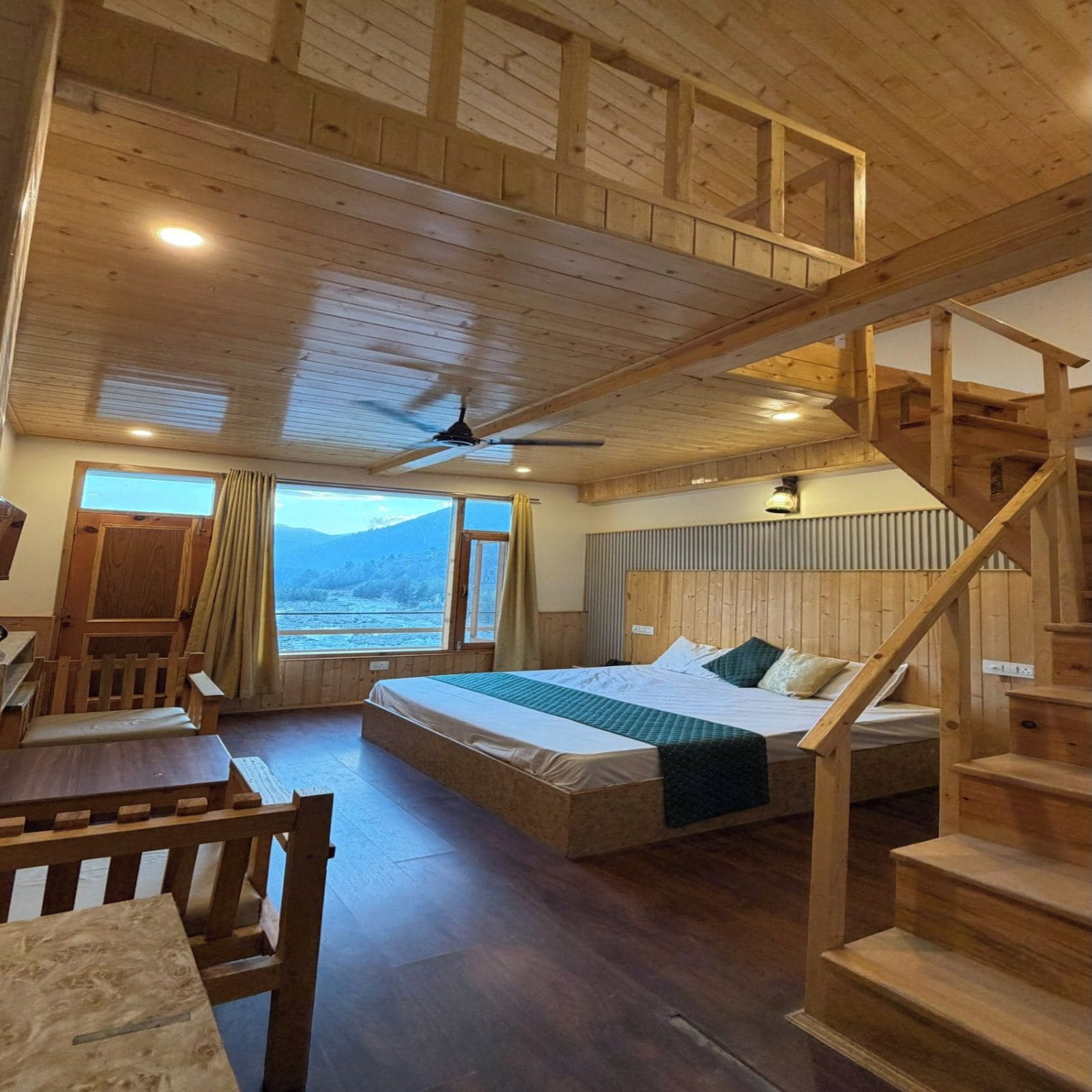 A wooden cabin interior with a bed, a desk, and a staircase.