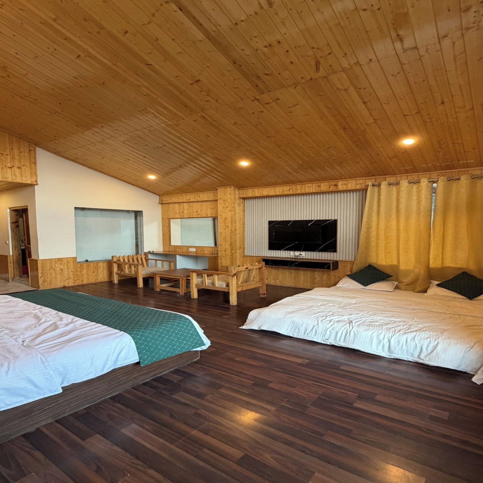 A room with two beds, a desk, a television, and a window with curtains.