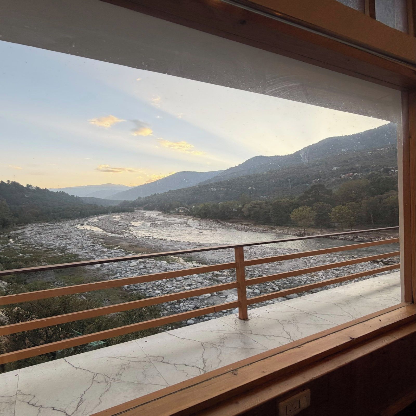A view from a window with a railing, overlooking a river and mountains.