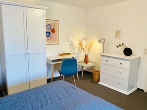 Ein Schlafzimmer mit einem Bett, einem Schreibtisch, einem Stuhl, einer Kommode und einem Bild an der Wand.