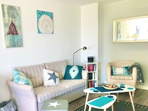 En stue med en stribet sofa, et lille sofabord, en bogreol og en stol med pude.