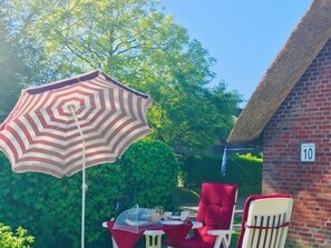 Eine Terrasse mit Tisch, Stühlen und einem gestreiften Sonnenschirm.
