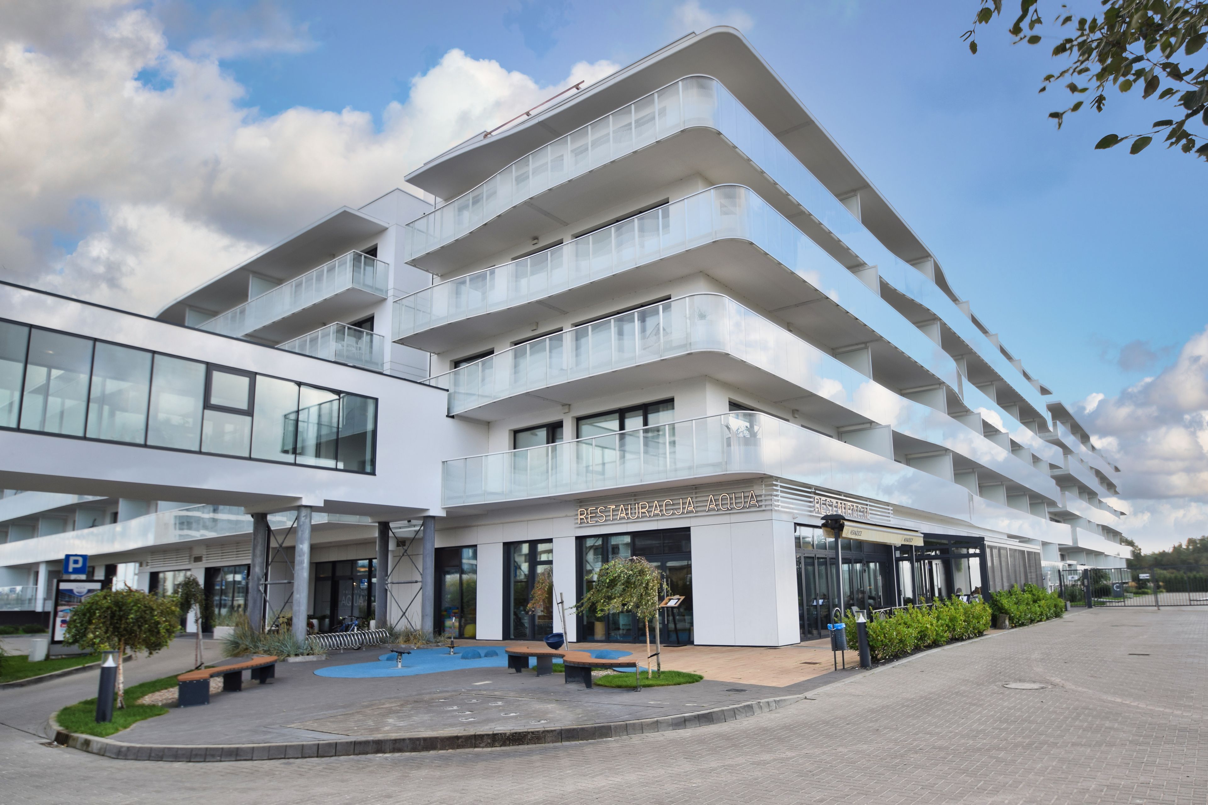 A modern multi-story hotel with a glass facade, outdoor seating area, and a clear sky.