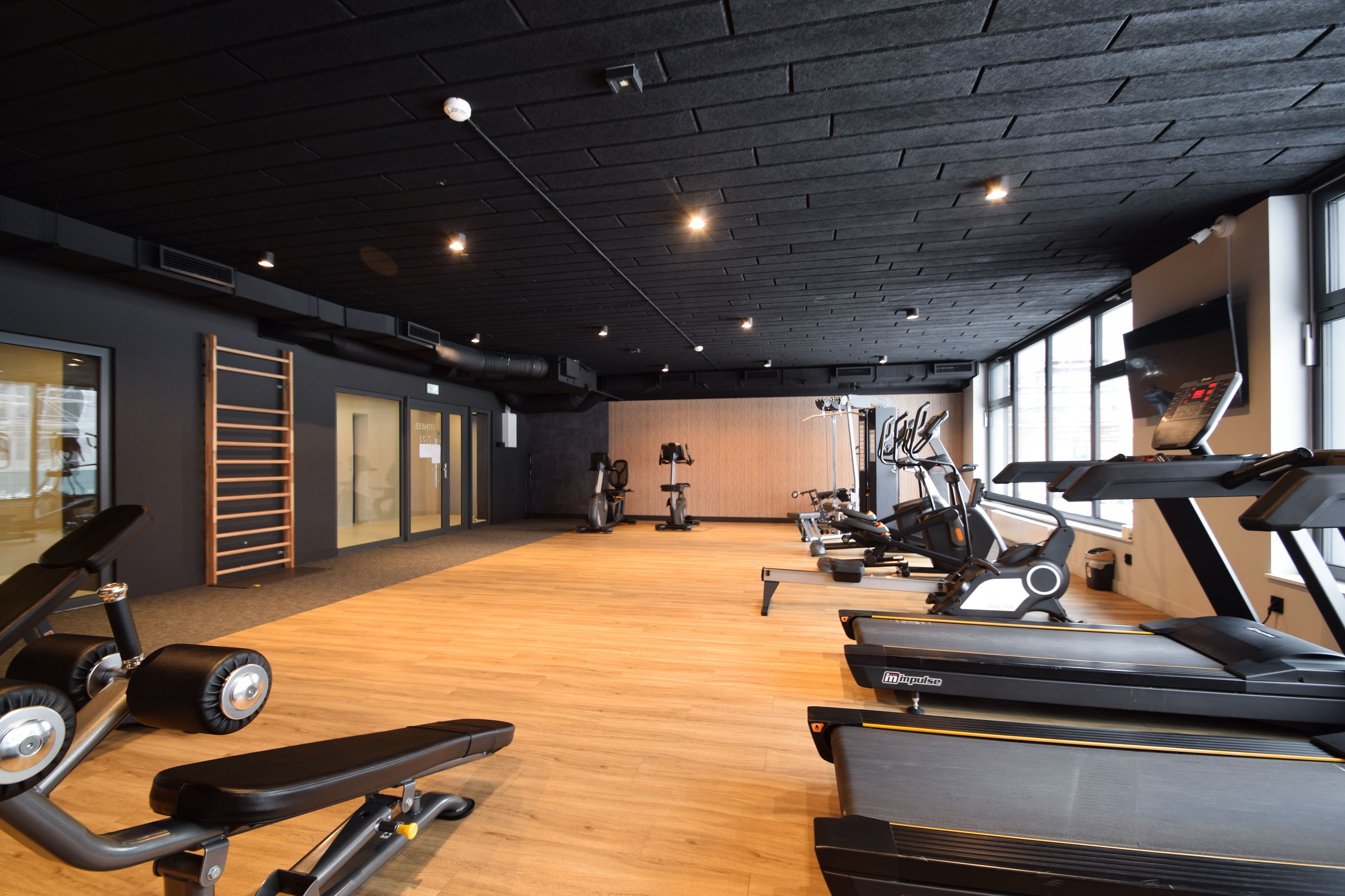Ein Fitnessraum mit verschiedenen Trainingsgeräten, darunter Laufbänder und Ergometer, sowie einem Holzboden.
