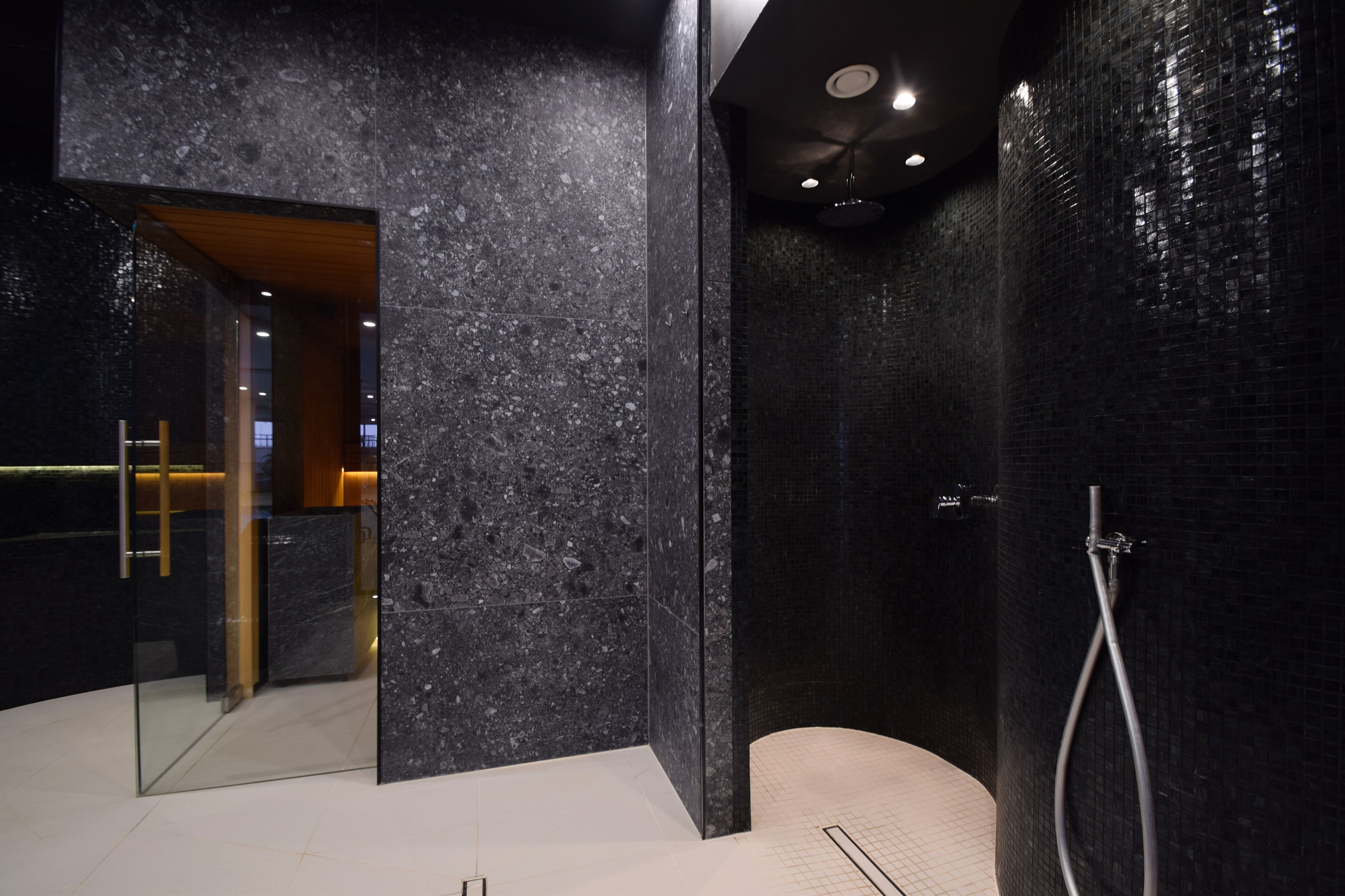 Ein modernes Badezimmer mit einer Duschkabine aus Glas, einer Marmorwand und einem sichtbaren Waschtisch.