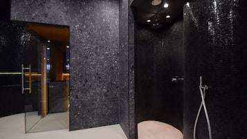 Ein modernes Badezimmer mit einer Duschkabine aus Glas, einer Marmorwand und einem sichtbaren Waschtisch.