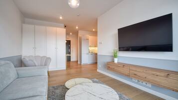 A modern living room with a grey sofa, a marble coffee table, a flat-screen TV mounted on the wall, and a wooden cabinet below.