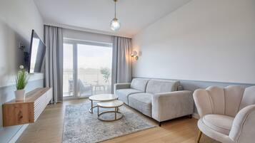 A modern living room with a sofa, armchair, TV, and a view through the window.