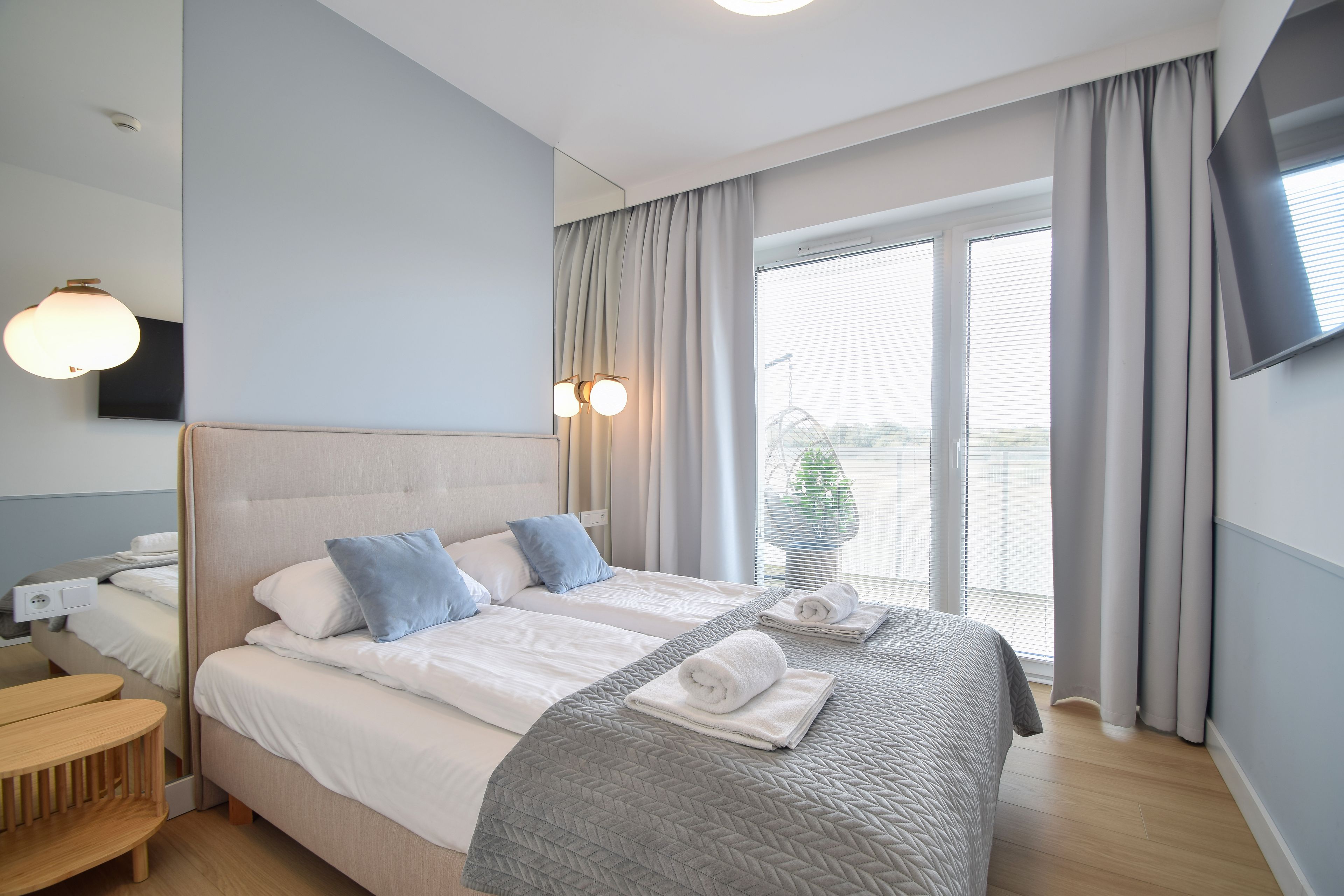 A hotel room with a bed, bedside table, and a TV mounted on the wall.