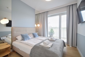 A hotel room with a bed, bedside table, and a TV mounted on the wall. - RentPlanet - Apartamenty Wydmowa (Kołobrzeg)