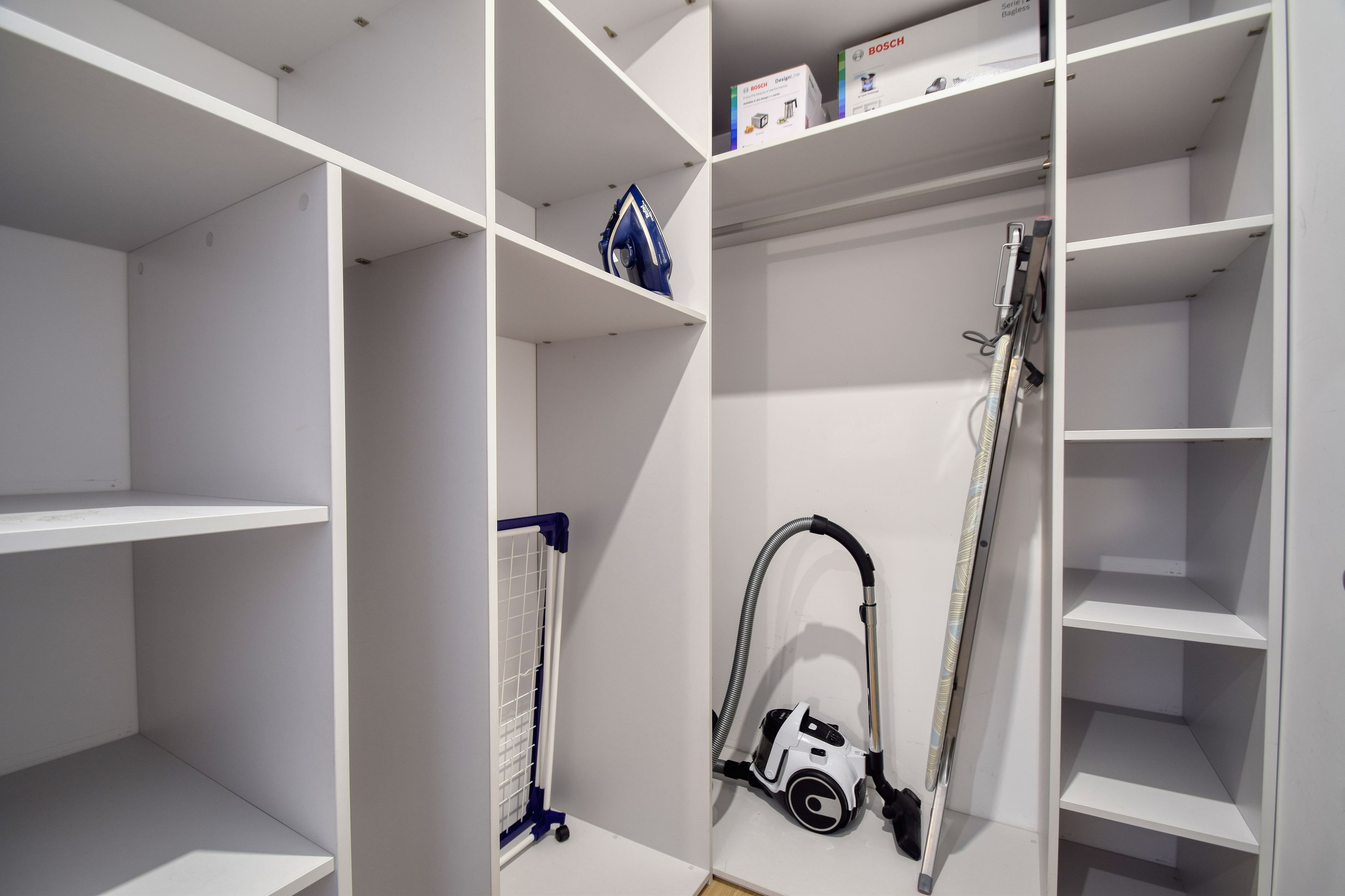 Ein Abstellraum mit Regalen, einem Staubsauger und einem Wäschekorb.