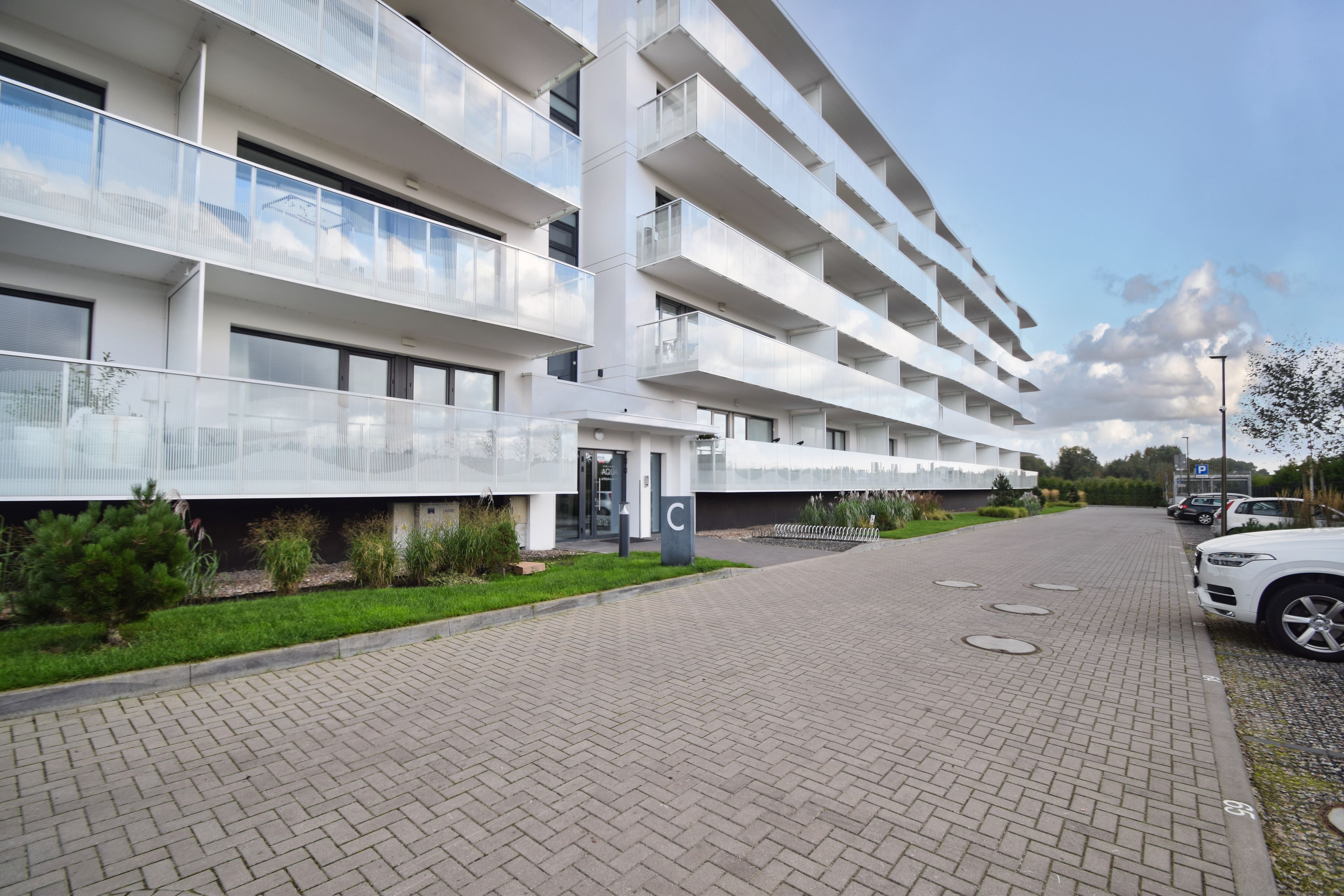 Un immeuble résidentiel à plusieurs étages, doté de balcons, d’une allée pavée et d’un espace de stationnement.