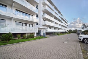 A multi-story residential building with balconies, a paved driveway, and a parking area. - RentPlanet - Apartamenty Wydmowa (Kołobrzeg)