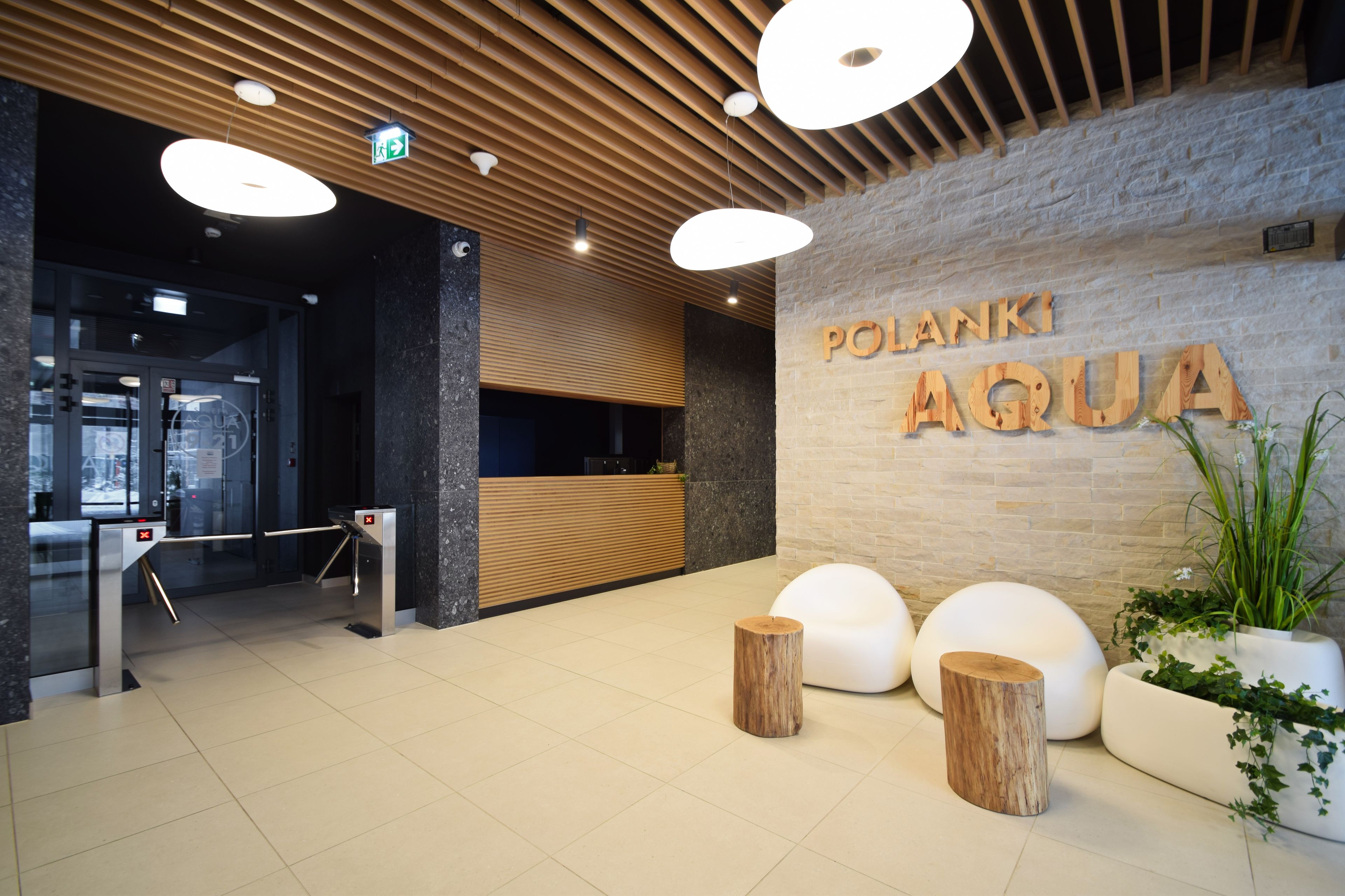 Un espace d’accueil doté d’un comptoir de réception en bois, d’une enseigne indiquant « POLANKI AGUA » et d’un aménagement intérieur moderne avec un mur en pierre et des éléments décoratifs en bois.