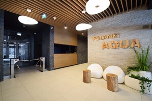A reception area with a wooden reception desk, a sign reading 'POLANKI AGUA', and a modern interior design with a stone wall and wooden accents. - RentPlanet - Apartamenty Wydmowa (Kołobrzeg)