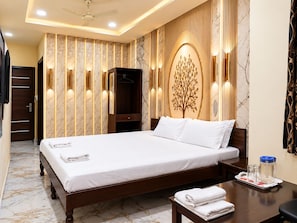 Habitación de hotel con una cama grande, un armario, un espejo, una decoración de árbol montada en la pared y una mesita de noche con una bandeja de toallas.