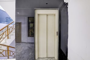 Una puerta de ascensor blanca con un panel de control, una escalera de madera y un cuadro en la pared.
