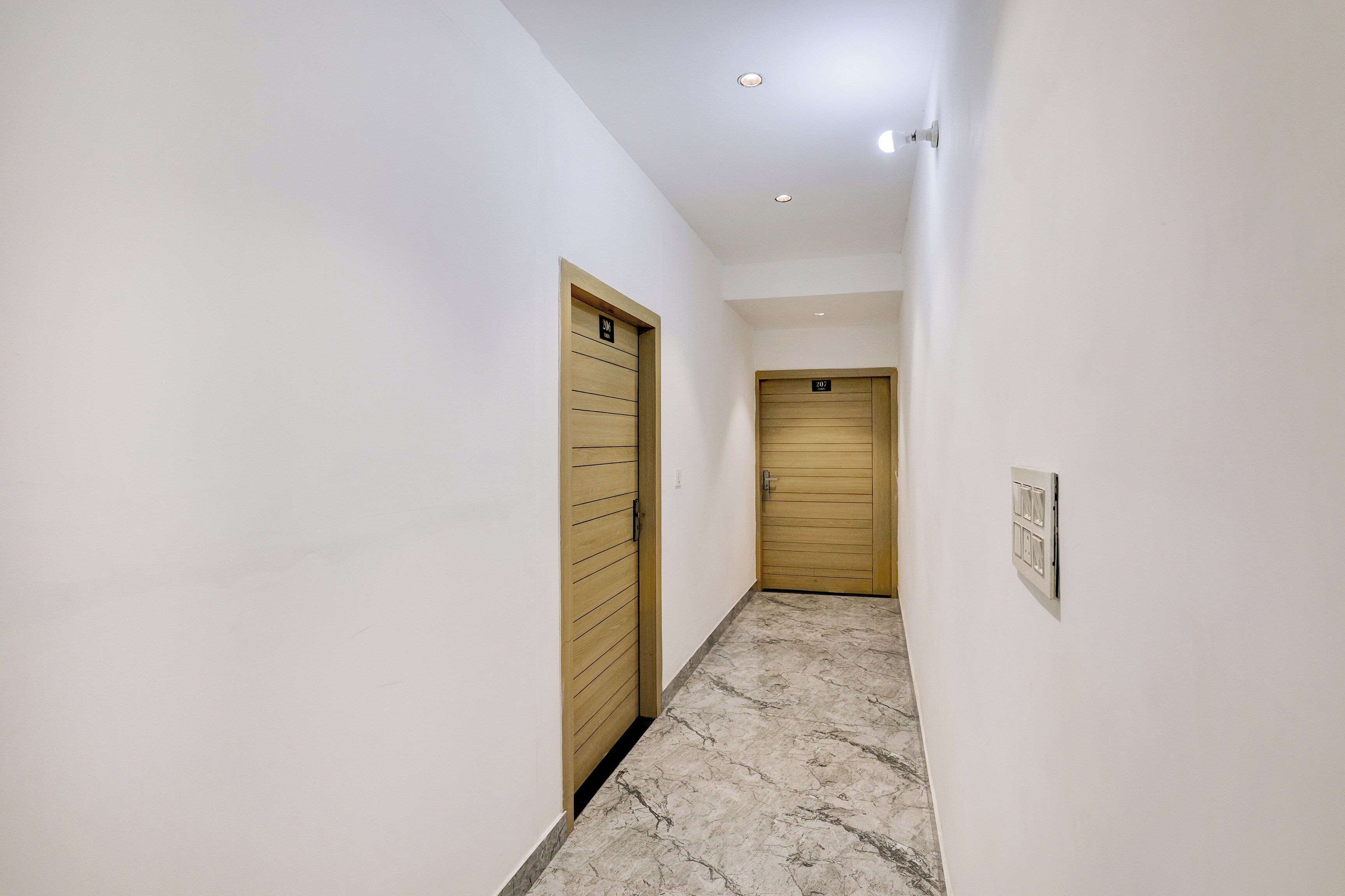 Un pasillo estrecho con dos puertas de madera, cada una marcada con un número. El suelo está cubierto de baldosas con un diseño de mármol.