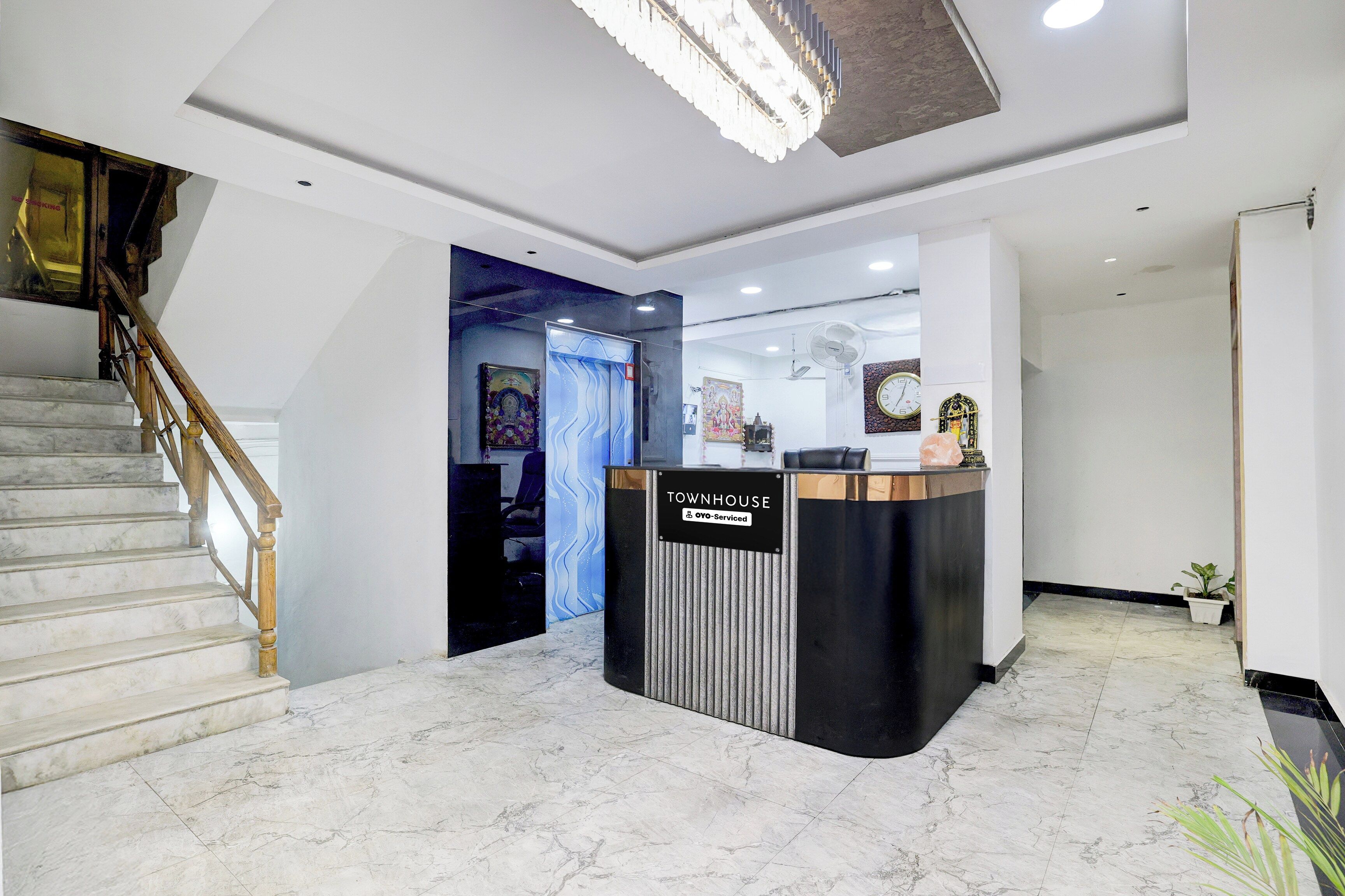 Zona de recepción con suelo de mármol, mostrador de recepción, escalera y lámpara en el techo.