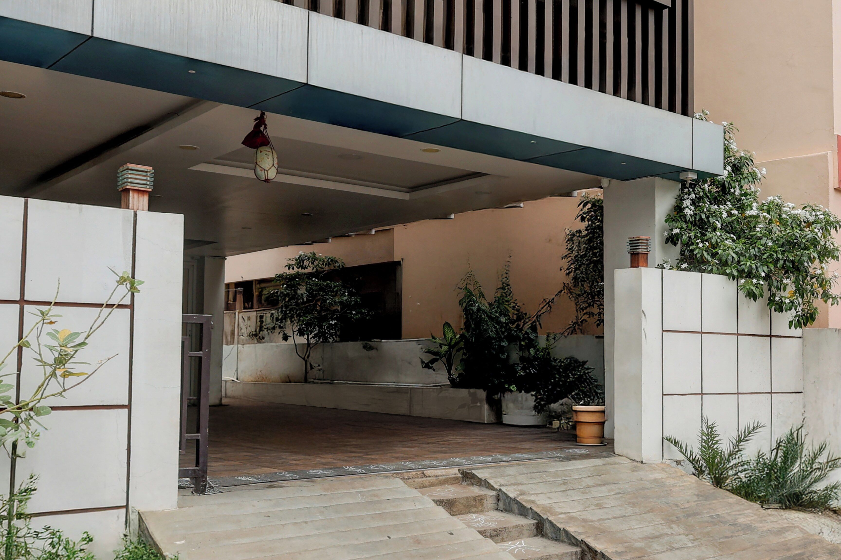 Entrada moderna de un edificio con fachada de hormigón, una escalera que sube a un área cubierta y plantas en macetas.