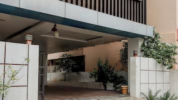 Entrada moderna de un edificio con fachada de hormigón, una escalera que sube a un área cubierta y plantas en macetas.