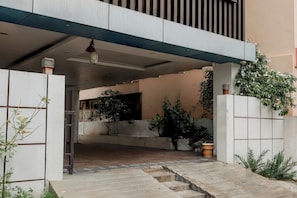 Entrada d'un edifici modern amb façana de formigó, escales que condueixen a una zona coberta i plantes en testos.