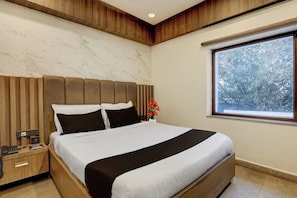 Habitación de hotel con una cama grande, cabecera de madera, una mesita de noche y una ventana con vistas a árboles.