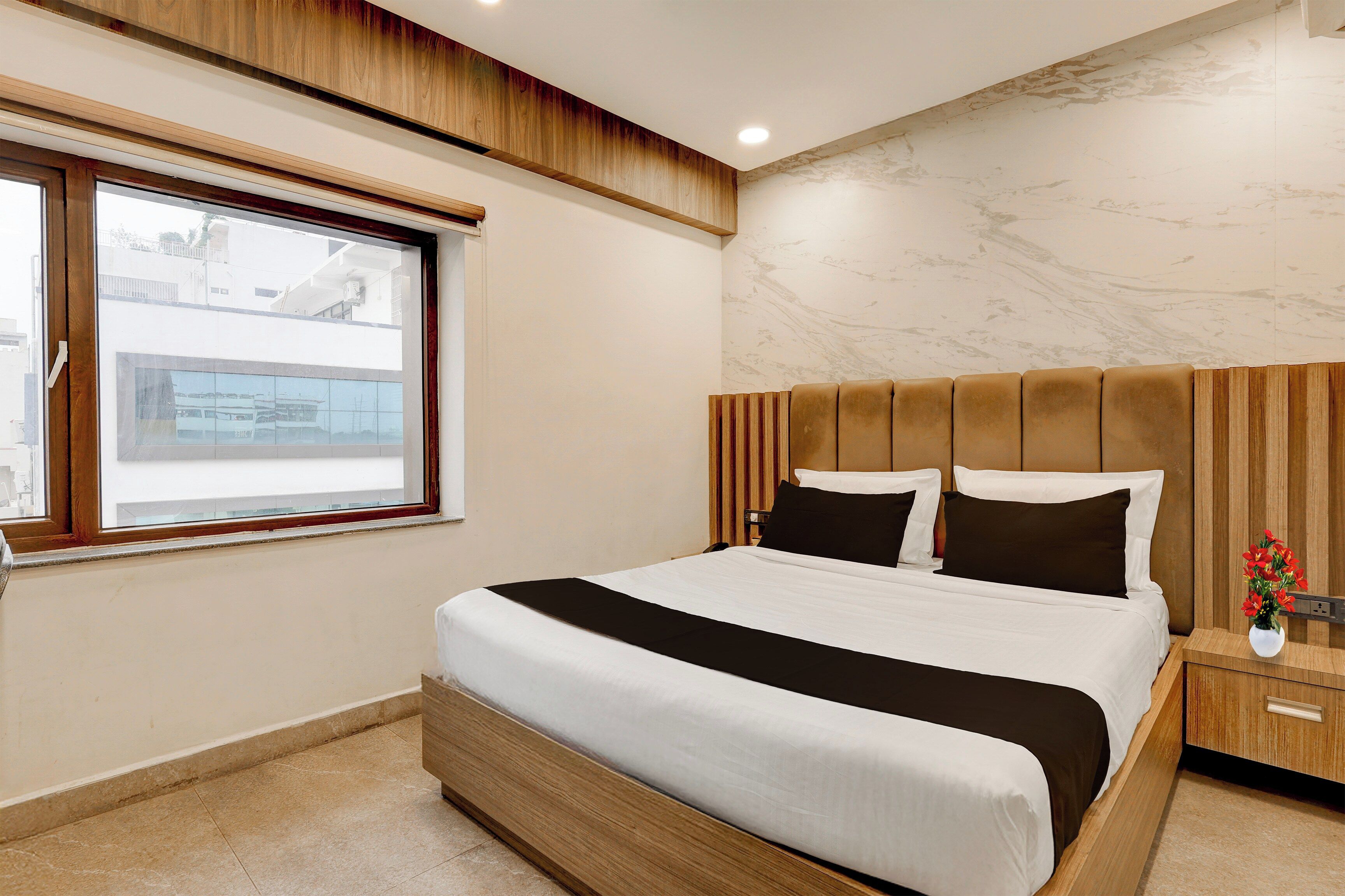 Habitación de hotel moderna con una cama grande, cabecera de madera, pared de mármol y ventana con vistas a edificios.