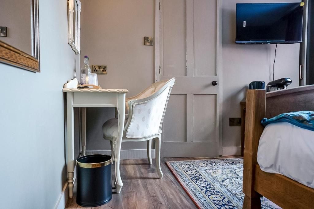 A bedroom with a bed, a desk with a chair, a television, and a patterned rug.