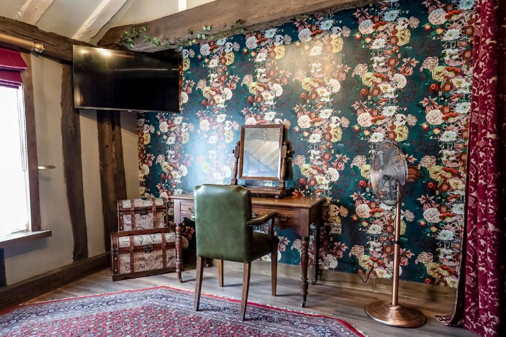 A room with a floral wallpaper, a desk with a mirror, a vintage fan, and a trunk.