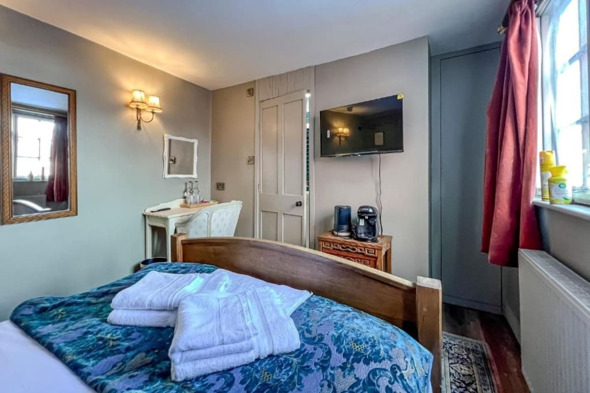 Een hotelkamer met een bed, een bureau, een stoel, een televisie en een raam met gordijnen.