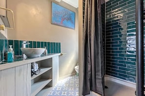 Een badkamer met een wit wastafelmeubel, een spiegel, een handdoekhouder, een douchegordijn en een wand betegeld met blauwe tegels.