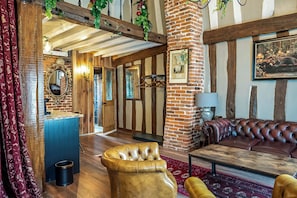 Een kamer met zichtbare bakstenen muren, een houten plafond, een leren bank, een gestoffeerde fauteuil en een houten salontafel.