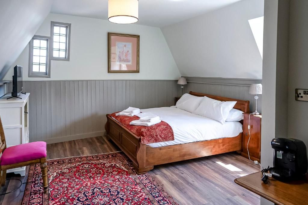 Une chambre avec un lit en bois, un bureau avec une chaise, un tapis rouge à motifs et un tableau encadré au mur.