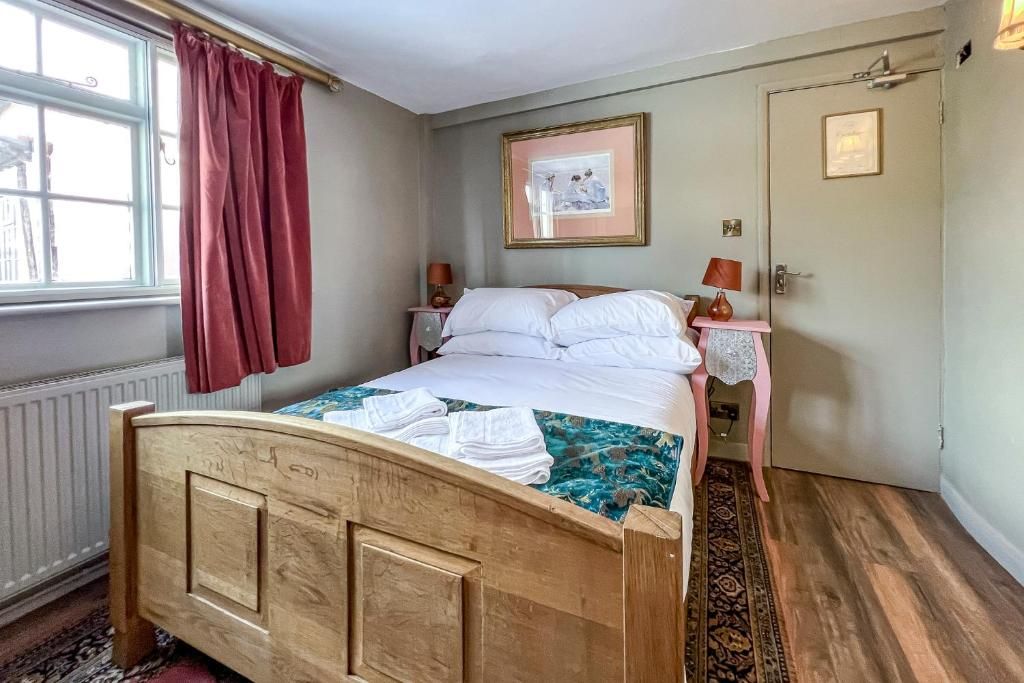 A bedroom with a wooden bed, a bedside table with a lamp, a framed picture on the wall, and a door with a small plaque.