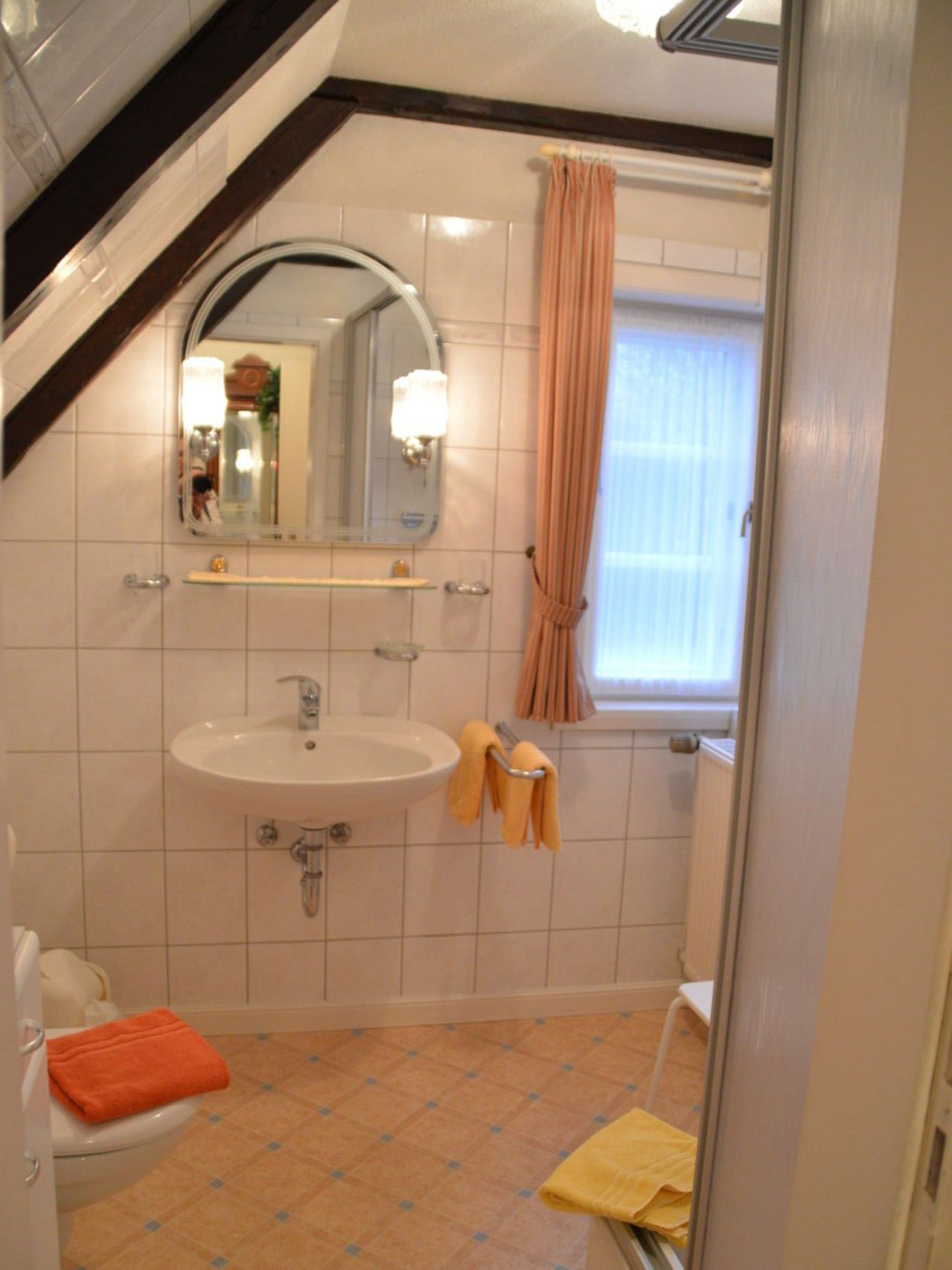 A bathroom with a white sink, a mirror, a towel rack, and a window with curtains.