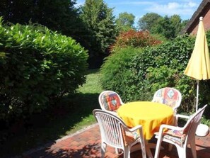 Eine Terrasse mit Tisch und Stühlen, umgeben von viel Grün.