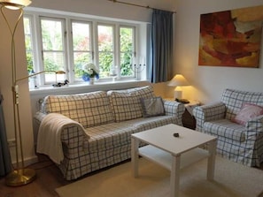 Ein Wohnzimmer mit einer Sofagarnitur, einem Couchtisch, einer Stehlampe und einem Bild an der Wand.