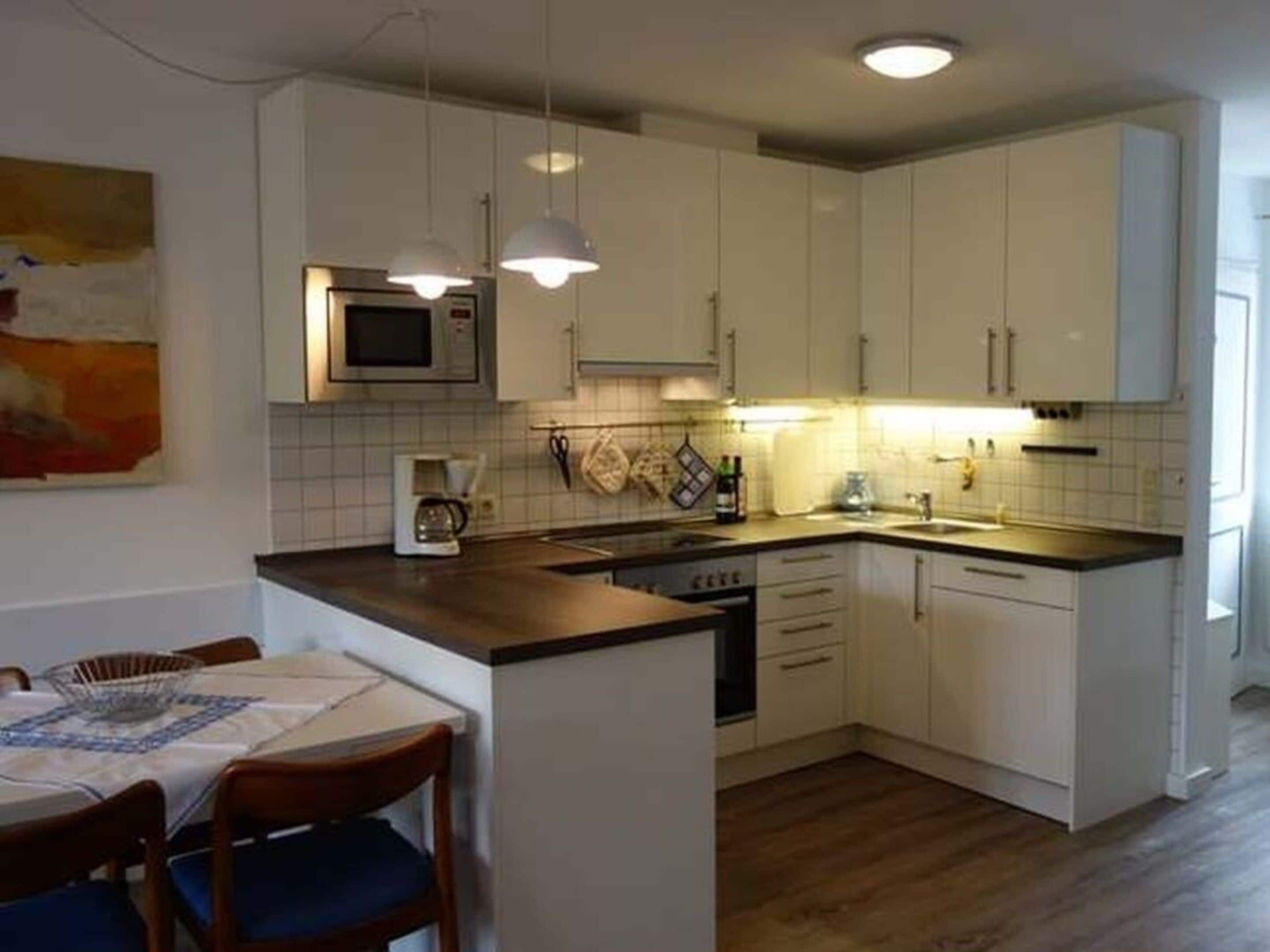 A compact kitchen with white cabinets, a microwave, a coffee maker, and a sink.