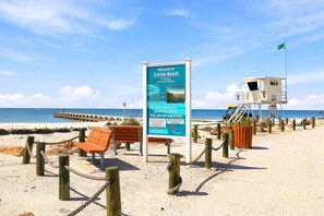 Una spiaggia con una torretta di salvataggio, un cartello che indica i servizi e una recinzione in legno.