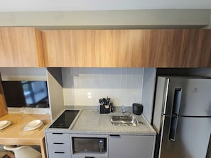 A compact kitchen with wooden cabinets, a built-in microwave, a stainless steel refrigerator, and a granite countertop. - Apartamento Conforto e Charme na Vila Cordeiro (São Paulo)