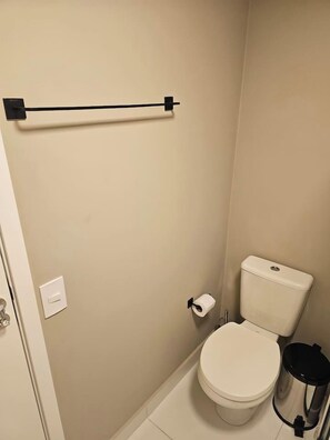 Un baño pequeño con un inodoro, un cubo de basura y un perchero para toallas.