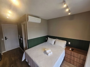 A hotel room with a bed, a nightstand, an air conditioning unit, and a door. - Apartamento Conforto e Charme na Vila Cordeiro (São Paulo)