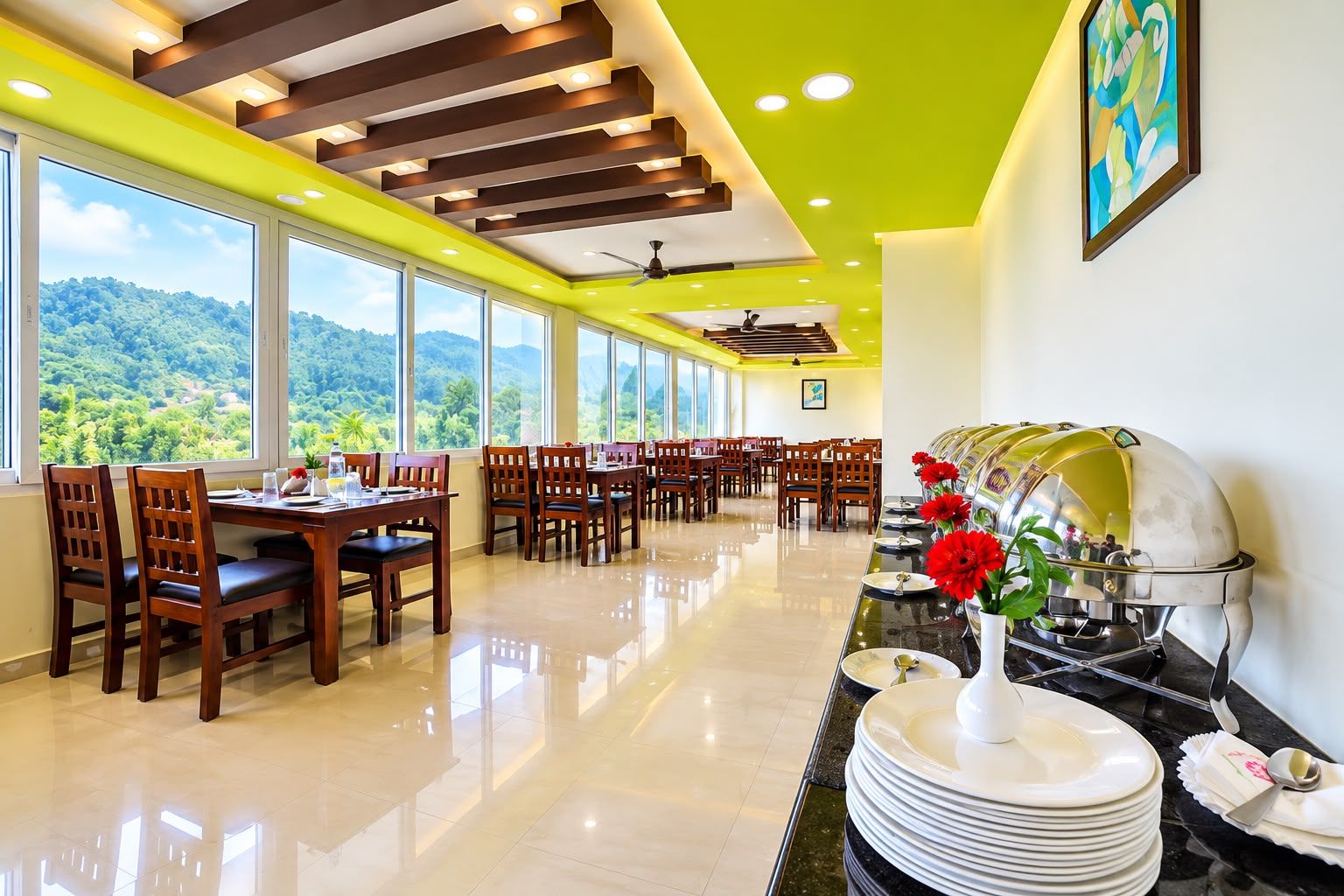 A hotel dining area with multiple tables and chairs, a buffet station with plates and cutlery, and large windows offering a view of the outdoors.