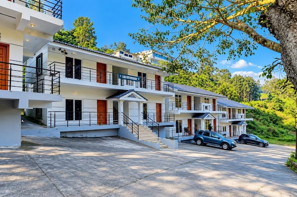 Un hotel de varios pisos con diseño moderno, con balcones, un estacionamiento y vistas al follaje circundante.