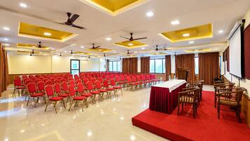 A conference room with rows of chairs, a stage, and ceiling fans.